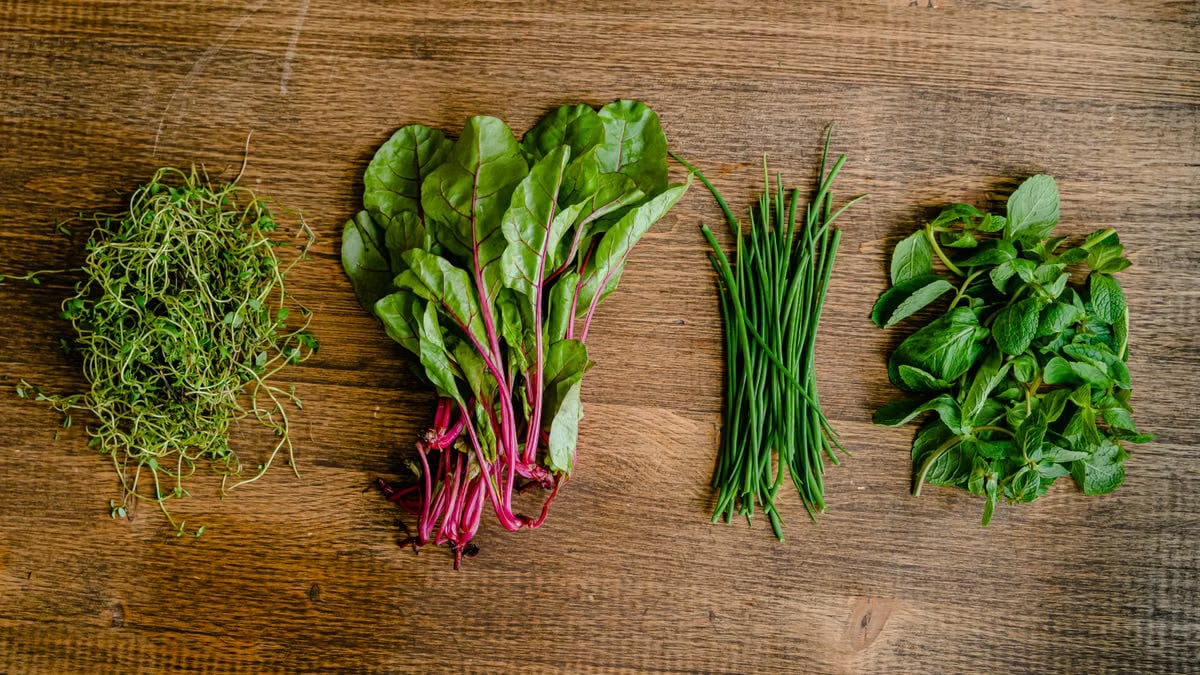 A vibrant selection of fresh herbs and greens neatly arranged on a wooden tabletop.